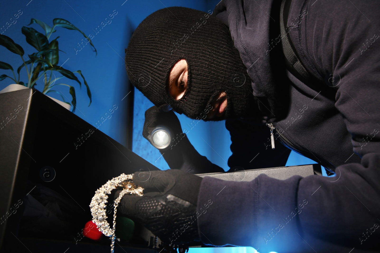 Photo of Thief taking jewelry out of steel safe indoors at night