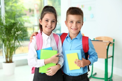 Photo of Cute little children with backpacks and school stationery in classroom