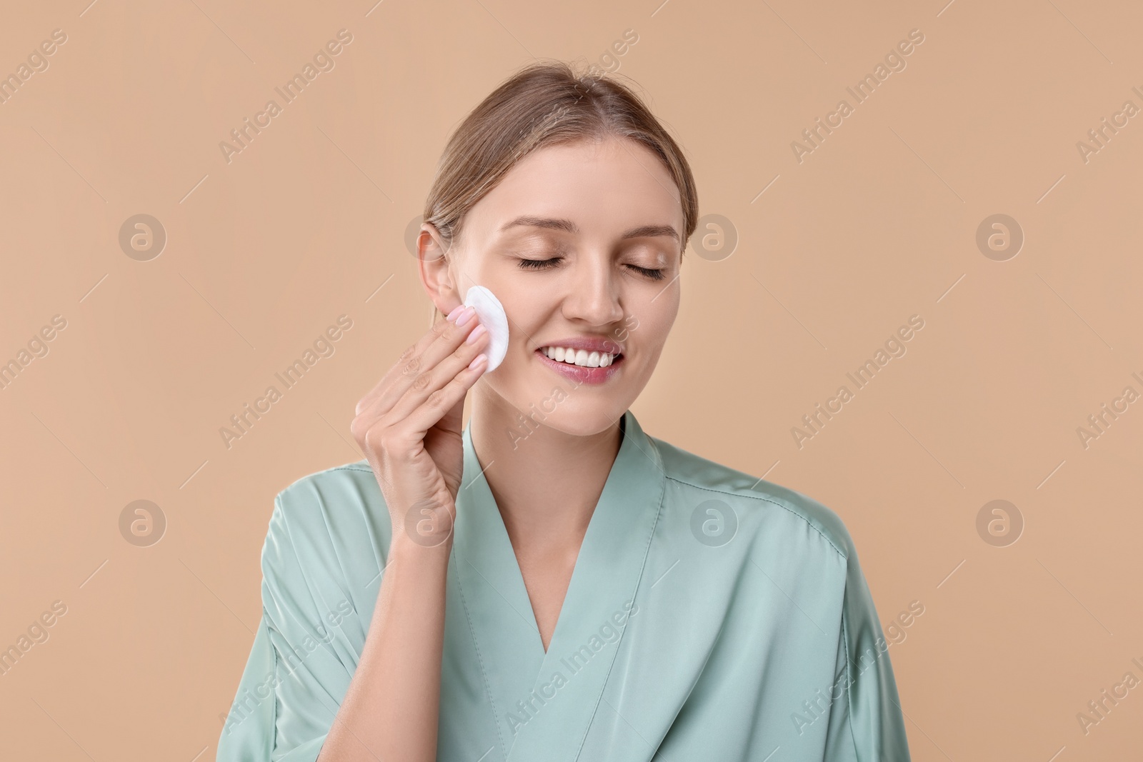 Photo of Young woman cleaning her face with cotton pad on beige background