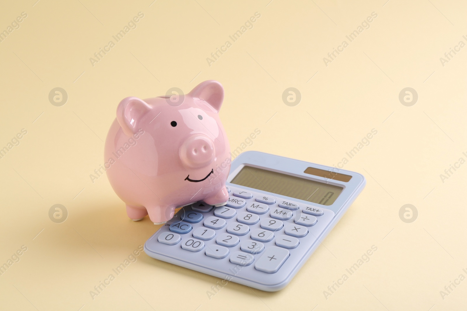 Photo of Financial savings. Piggy bank and calculator on beige background