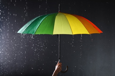 Photo of Woman holding bright umbrella under rain on dark background, closeup