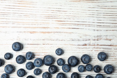 Photo of Fresh tasty blueberries on white wooden table, top view with space for text