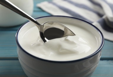 Photo of Eating tasty yogurt from bowl on light blue wooden table, closeup