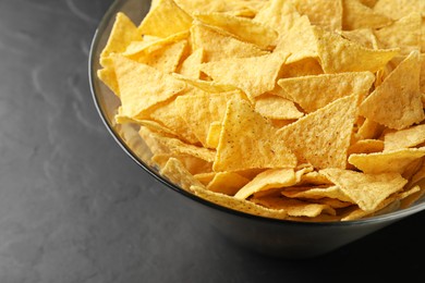 Photo of Glass bowl with tortilla chips (nachos) on black table, closeup