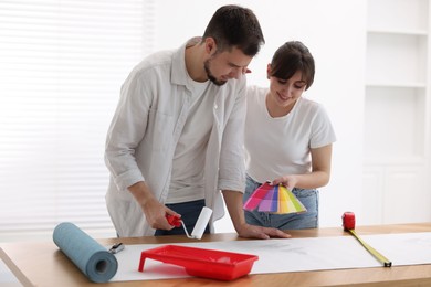 Photo of Woman and man applying glue onto wallpaper sheet at wooden table indoors