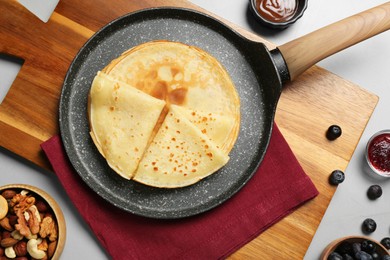 Photo of Delicious crepes with nuts and jam on light grey table, flat lay