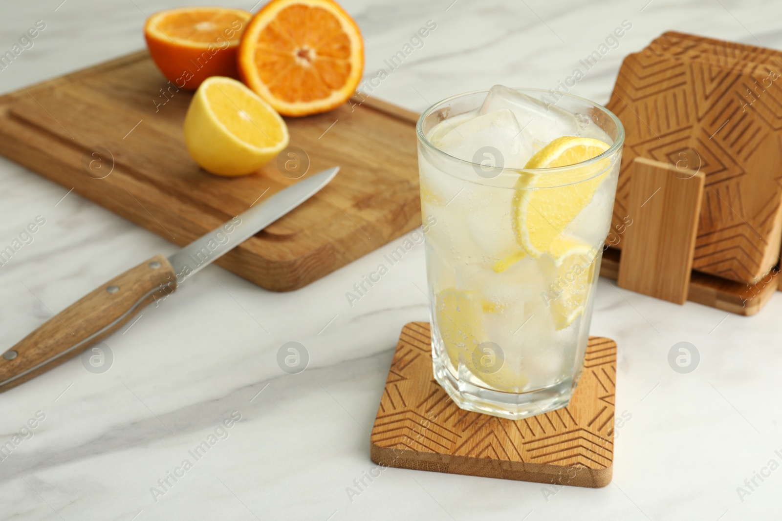 Photo of Glass of cocktail and stylish wooden cup coasters on white table