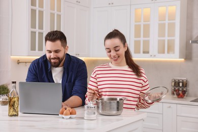 Happy lovely couple using laptop while cooking in kitchen