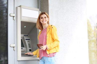 Photo of Beautiful woman using cash machine for money withdrawal outdoors. Space for text