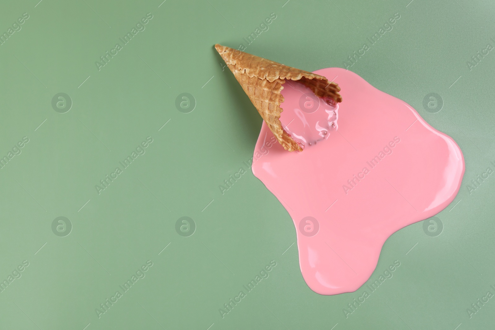 Photo of Melted ice cream and wafer cone on green background, top view. Space for text