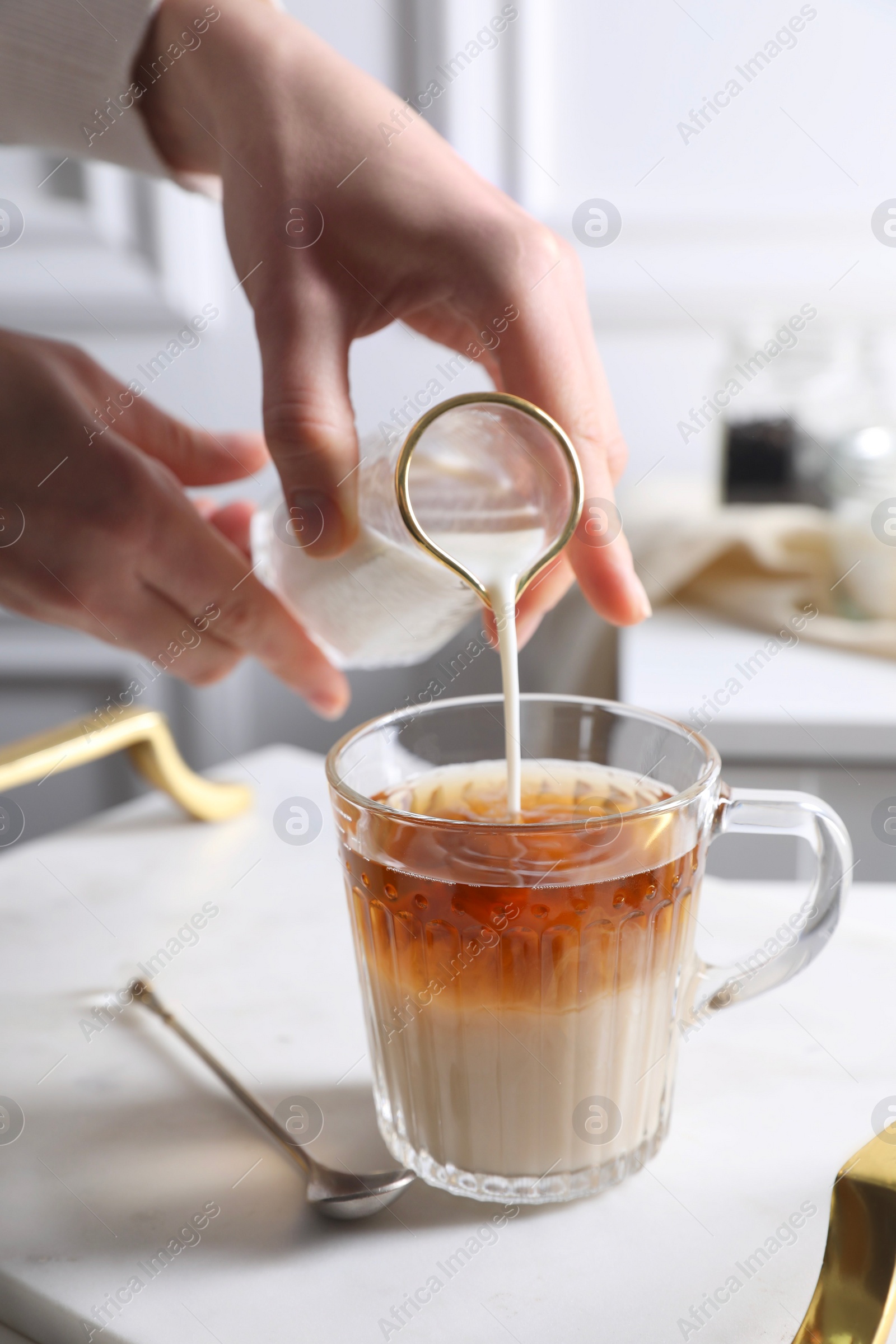 Photo of Woman pouring milk into cup of tea at white table, closeup