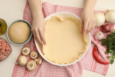 Photo of Woman putting dough for meat pie into baking dish at white wooden table, top view