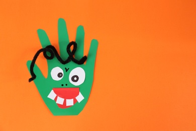 Photo of Funny green hand shaped monster on orange background, top view with space for text. Halloween decoration