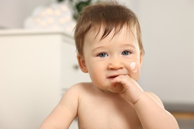 Photo of Cute little baby with moisturizing cream on face indoors