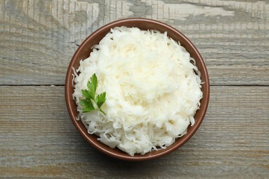 Photo of Tasty fermented cabbage with parsley on wooden table, top view