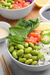Photo of Poke bowl with salmon, edamame beans and rice on light grey table, closeup