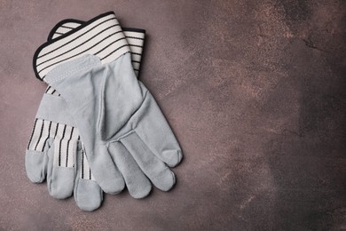 Photo of Pair of color gardening gloves on brown textured table, top view. Space for text