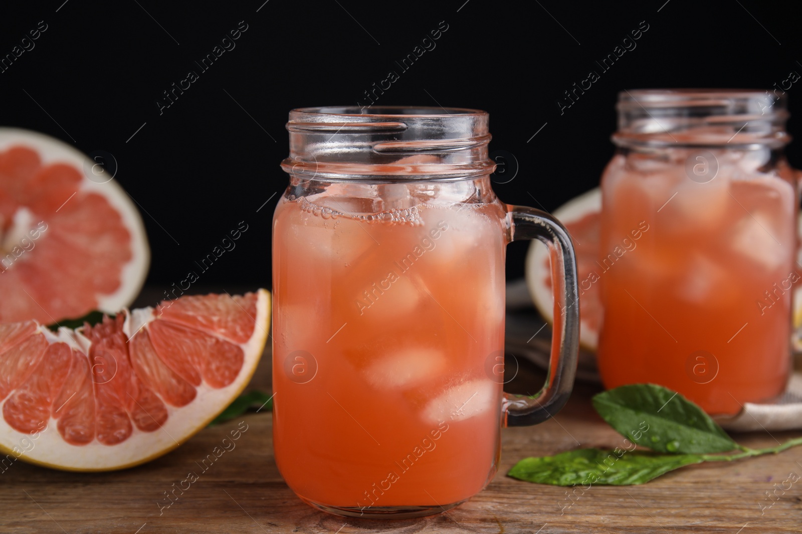 Photo of Glass jar with cold pomelo juice and fruit on wooden table against black background