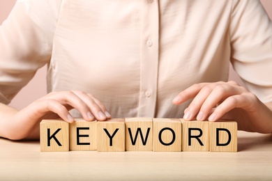 Woman demonstrating cubes with word KEYWORDS at wooden table, closeup