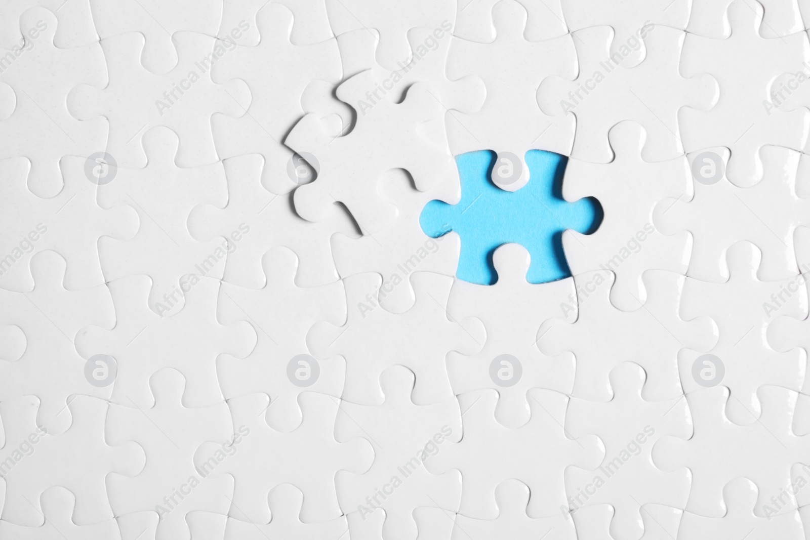 Photo of Blank white puzzle with separated piece on light blue background, top view