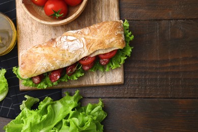 Delicious sandwich with sausages and vegetables on wooden table, flat lay. Space for text