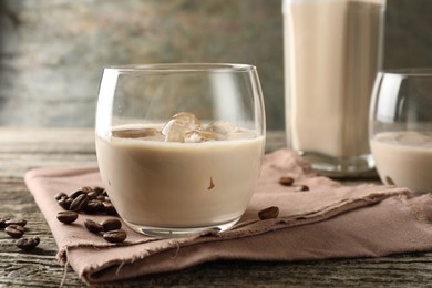 Photo of Coffee cream liqueur in glass and beans on wooden table, closeup