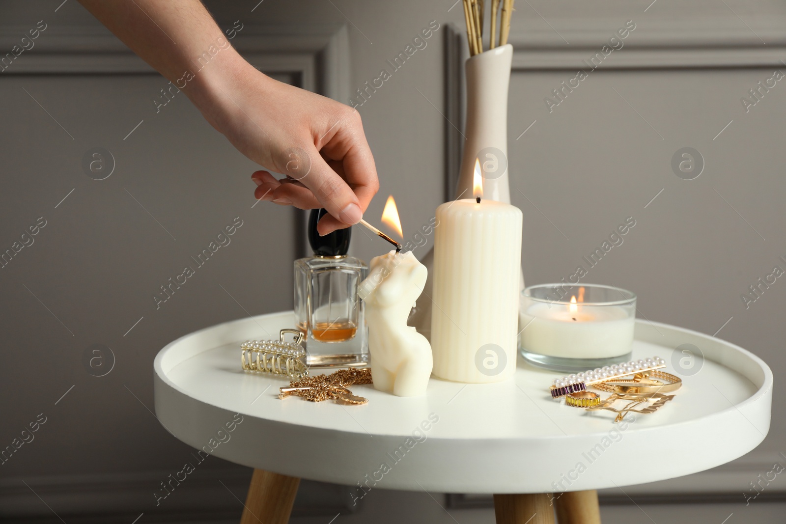 Photo of Woman lighting female body shaped candle on white table, closeup. Stylish decor