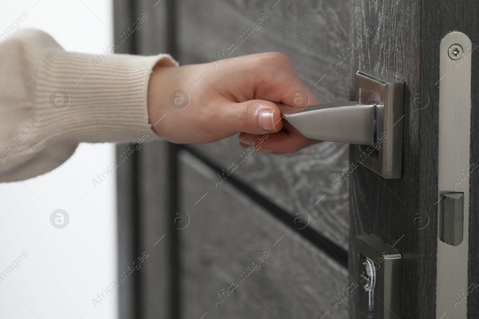 Photo of Woman opening wooden door indoors, closeup of hand on handle