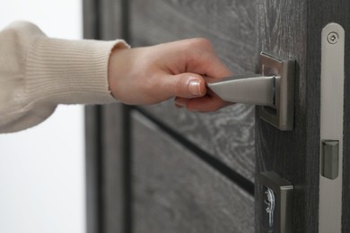 Photo of Woman opening wooden door indoors, closeup of hand on handle