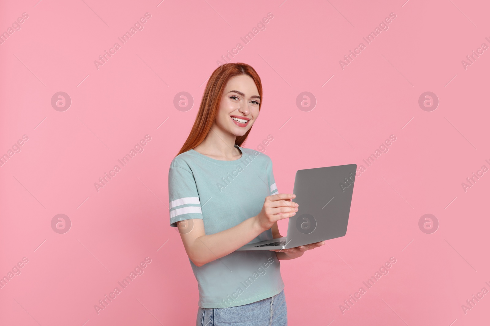 Photo of Smiling young woman with laptop on pink background