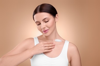 Photo of Beautiful woman with smear of body cream on her neck against light brown background