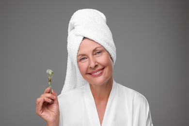 Photo of Woman with jade roller on grey background. Facial massage