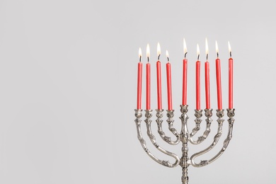 Photo of Silver menorah with burning candles on light grey background, space for text. Hanukkah celebration