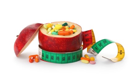 Photo of Cut apple full of weight loss pills and measuring tape on white background