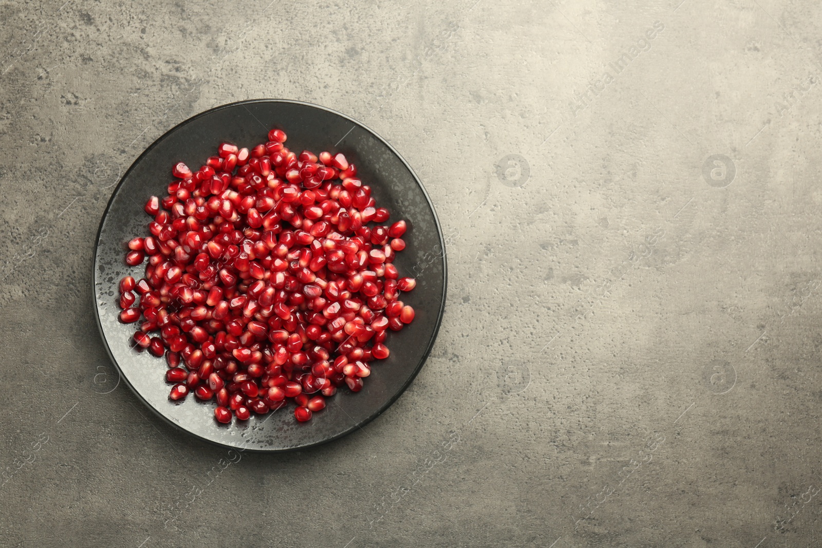 Photo of Ripe juicy pomegranate grains on grey textured table, top view. Space for text