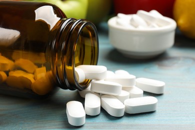 Photo of Dietary supplements. Overturned bottle with pills on light blue wooden table, closeup