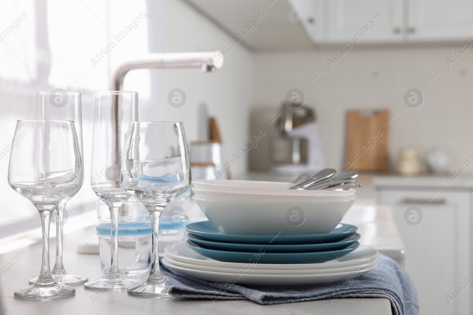 Photo of Different clean dishware, cutlery and glasses on countertop in kitchen