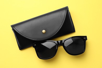 Photo of Stylish sunglasses and black leather case on yellow background, flat lay