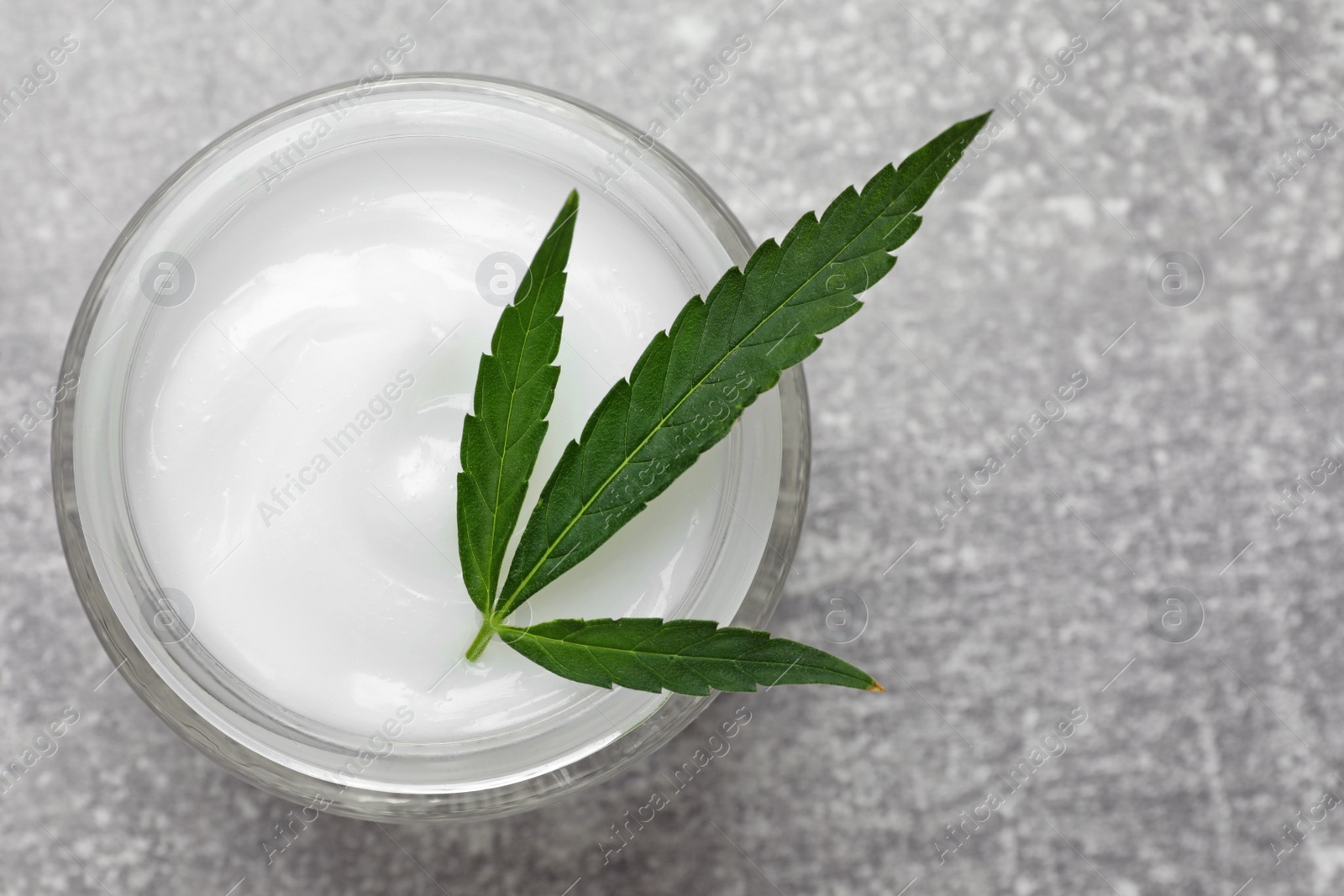 Photo of Jar of hemp cream and leaf on grey table, top view. Natural cosmetics