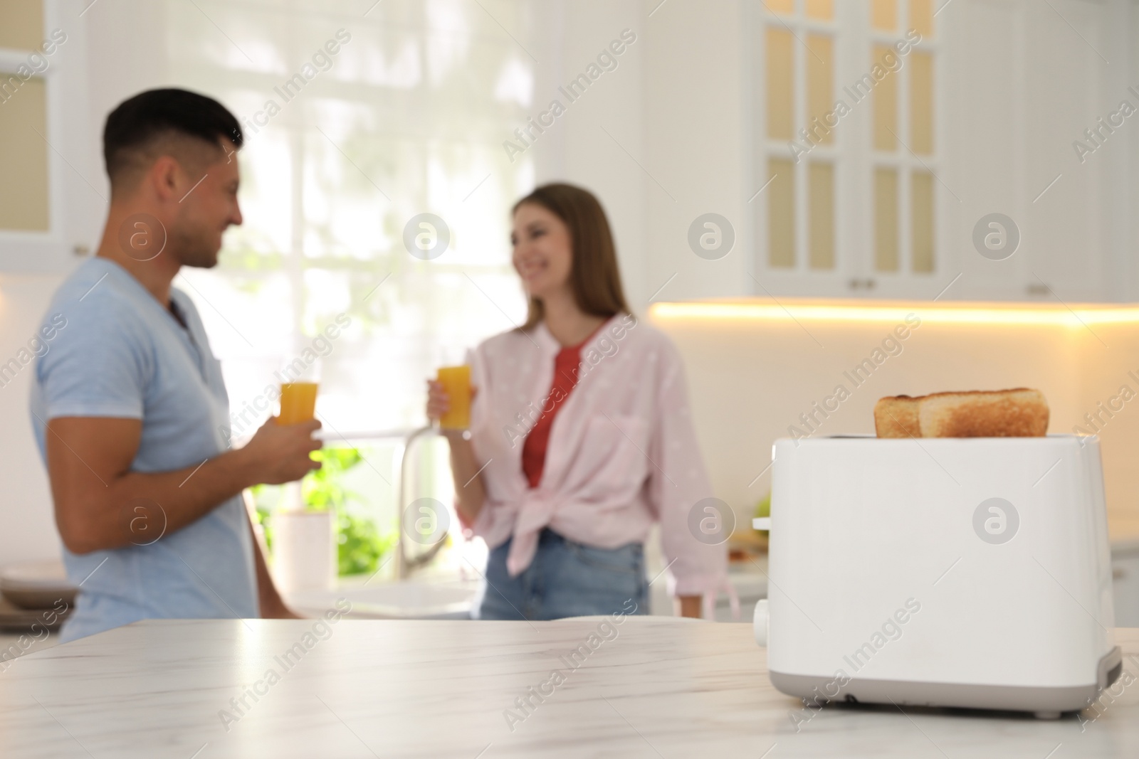 Photo of Modern toaster with slices of bread and blurred couple on background