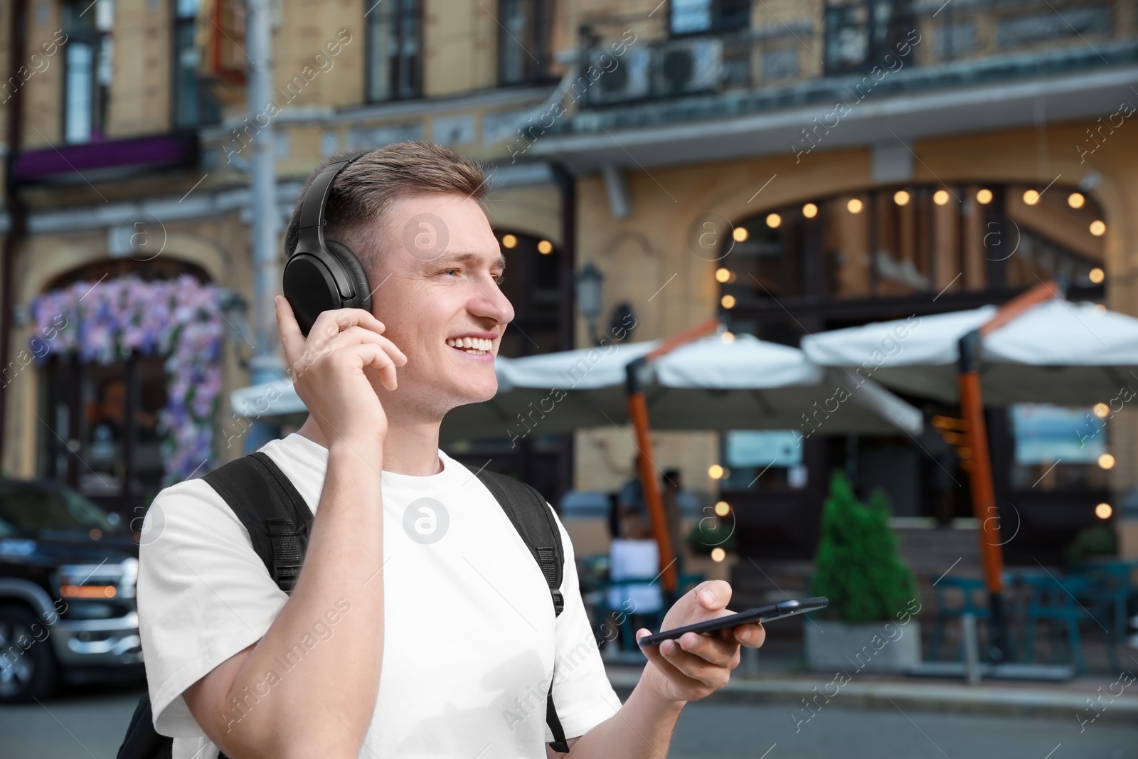 Photo of Smiling man in headphones using smartphone outdoors. Space for text