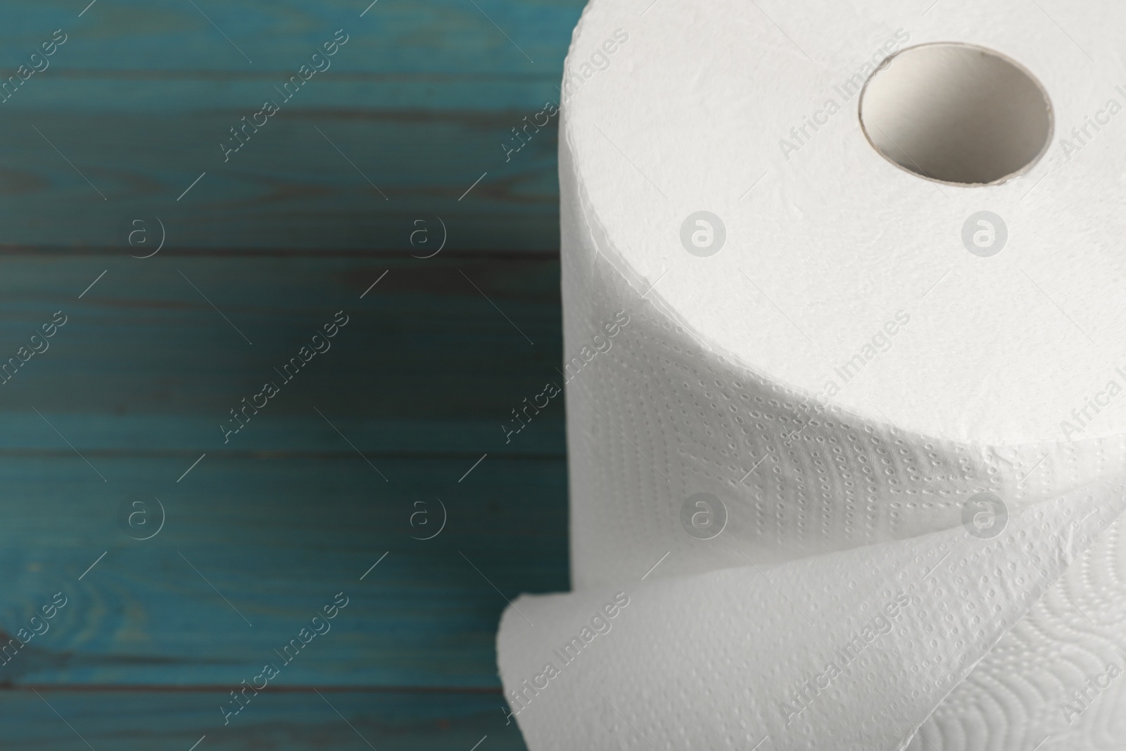 Photo of Roll of white paper towels on light blue wooden table, closeup. Space for text