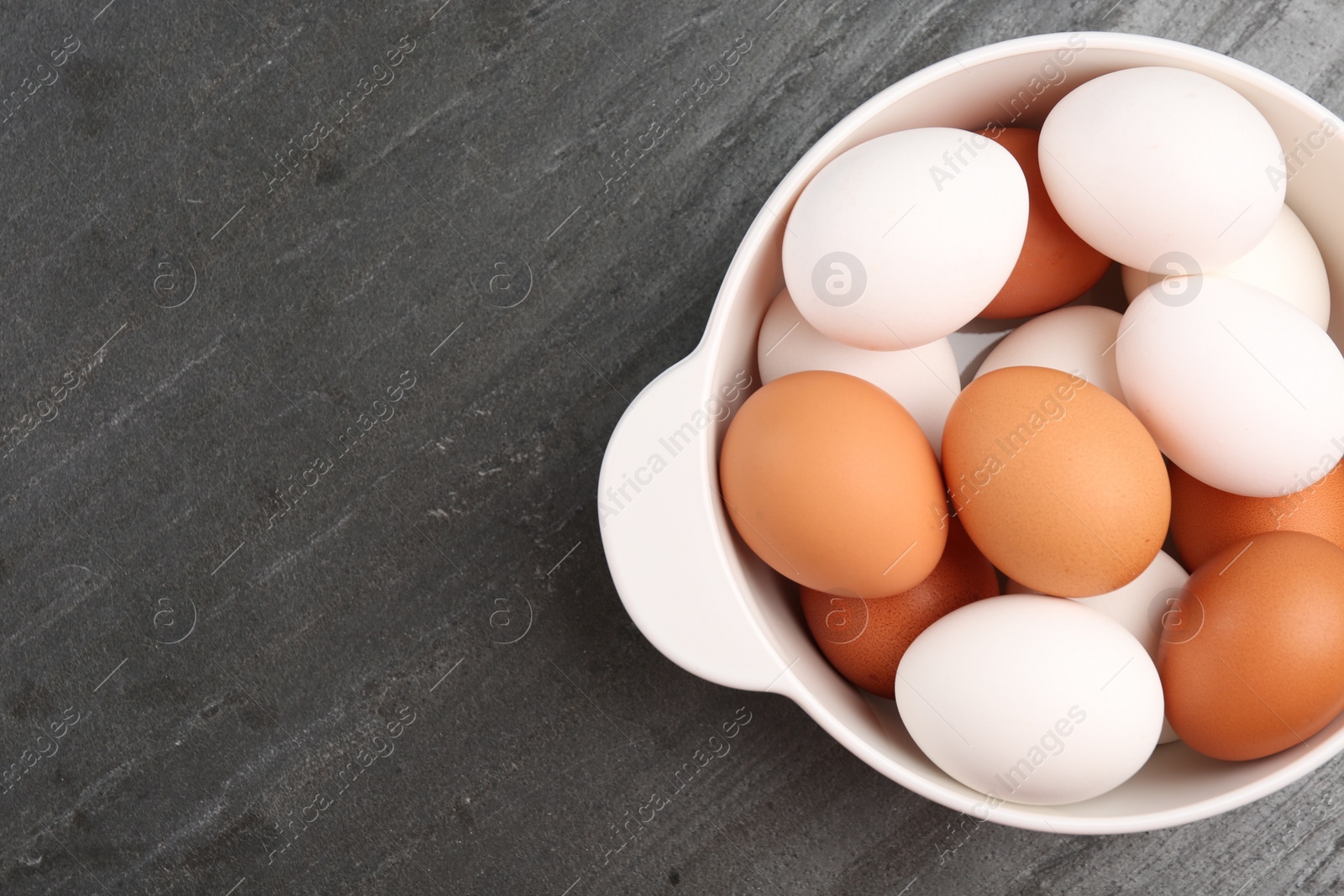 Photo of Unpeeled boiled eggs in saucepan on dark grey table, top view. Space for text