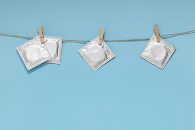 Clothesline with packaged condoms on light blue background, space for text. Safe sex