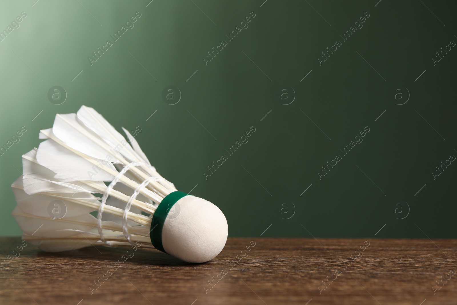 Photo of Feather badminton shuttlecock on wooden table against green background, closeup. Space for text