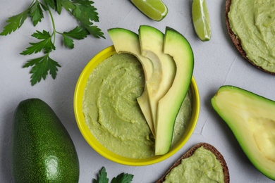 Flat lay composition with bowl of guacamole made of ripe avocados on grey table
