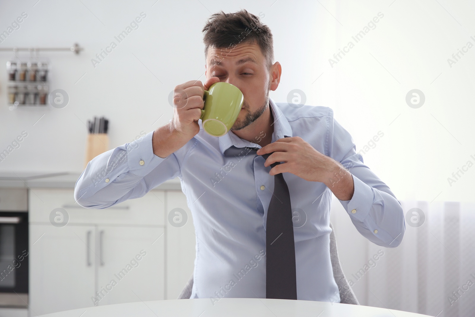 Photo of Sleepy man with cup of drink at home in morning