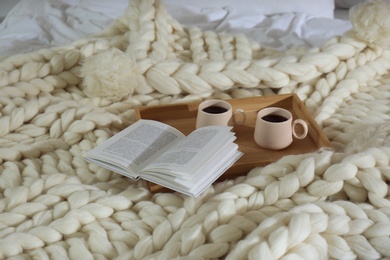 Photo of Wooden tray with cups and book on white knitted plaid
