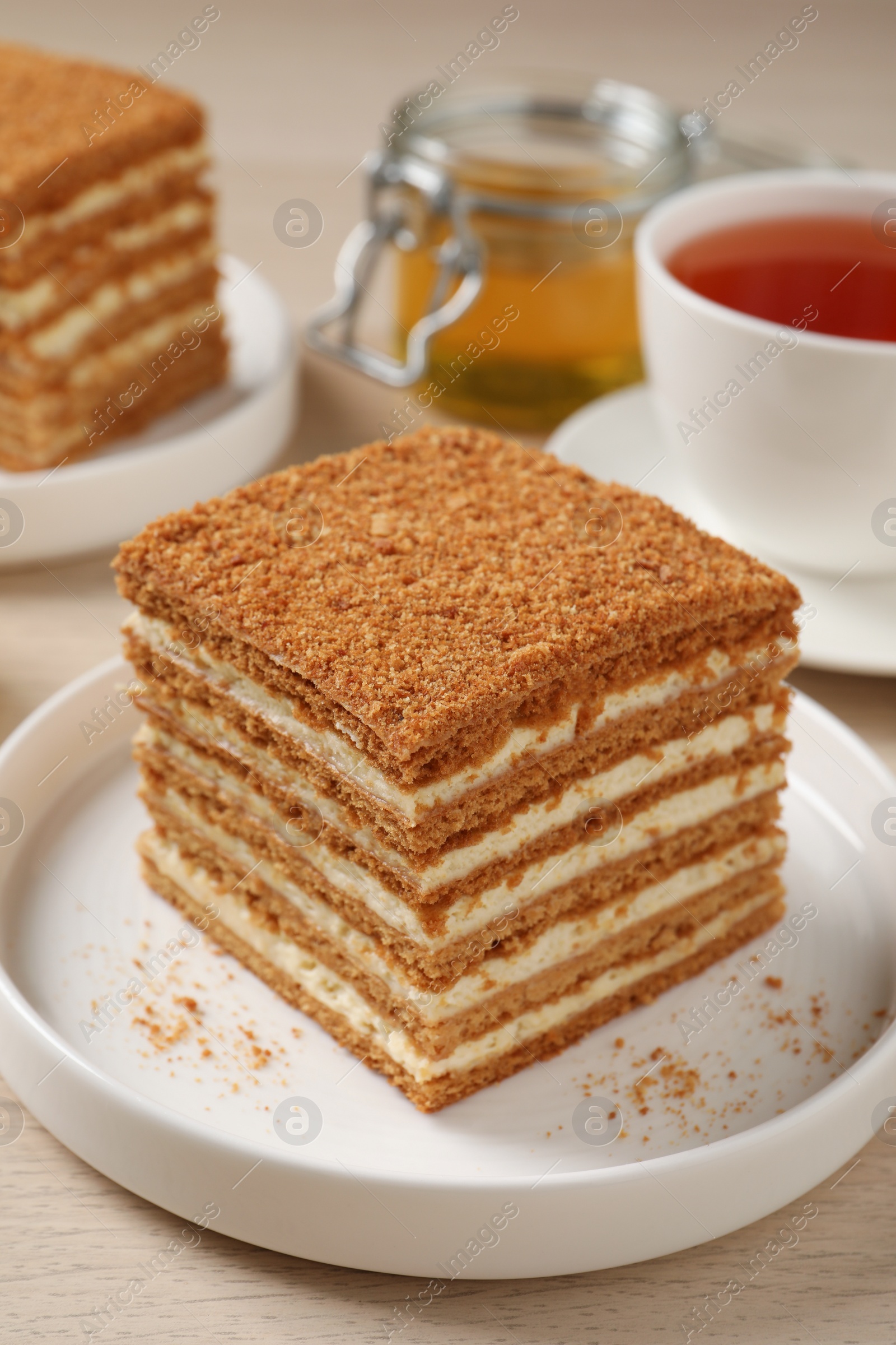 Photo of Delicious layered honey cake served with tea on wooden table, closeup