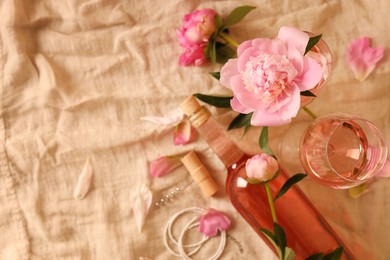 Flat lay composition with rose wine and beautiful peonies on beige fabric. Space for text